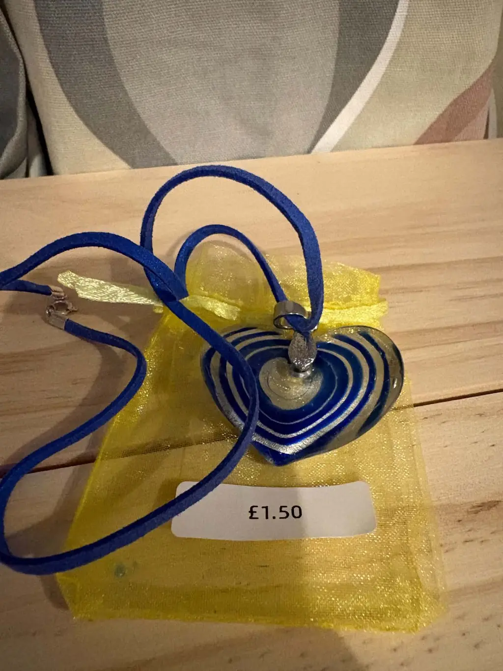 A blue and silver swirled glass heart pendant on a blue cord, on a yellow organza bag