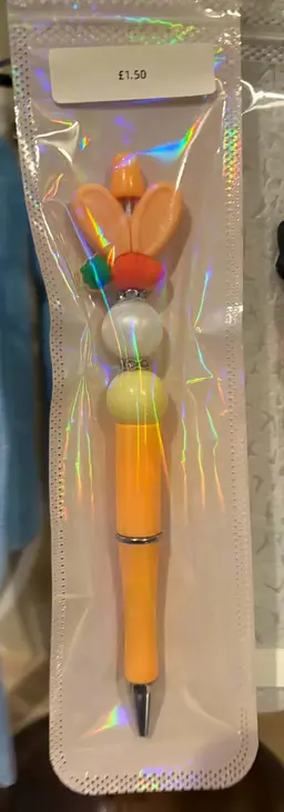 An orange beaded pen topped with bunny ears and a carrot, in a shiny pouch