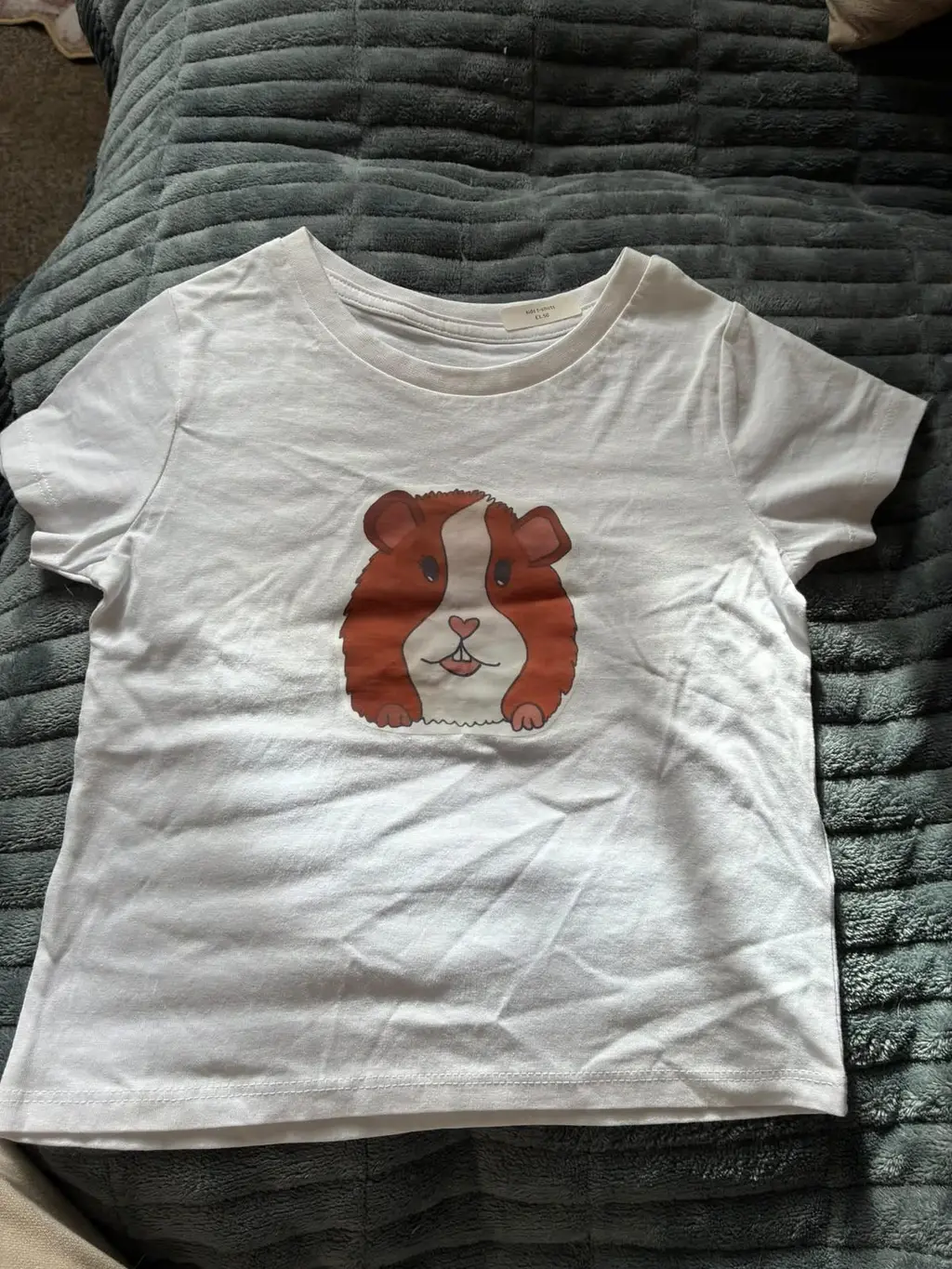 A white kids’ t-shirt printed with a ginger and white guinea pig